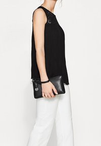 Un haut noir sans manches avec un détail en crochet au niveau de l'encolure, associé à un pantalon blanc et une pochette en cuir noire.