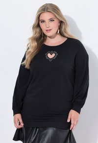 Sudadera negra con un corte de corazón en el centro, rodeado de cuentas decorativas. Mangas largas y un corte relajado con puños acanalados.