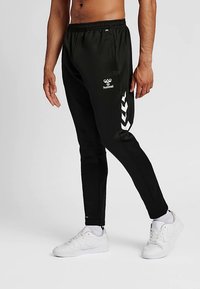 Czarne sportowe spodnie o zwężanym kroju, z elastycznym pasem i białym logo; z białymi wzorami typu jodełka po bokach.