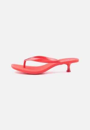 Rote Flip-Flop-Sandale mit gebogener Sohle und niedrigem Kittenabsatz auf weißem Hintergrund.