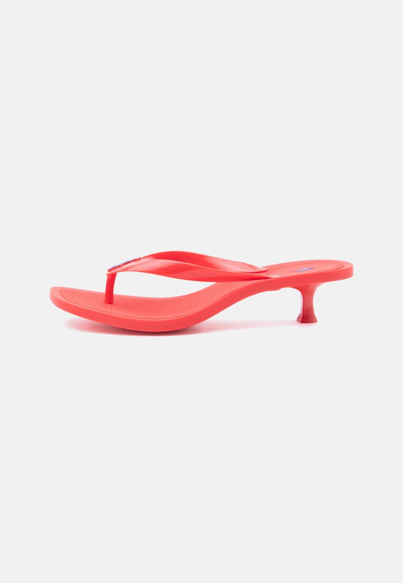 Sandale flip-flop rouge avec une semelle incurvée et un petit talon kitten sur fond blanc.