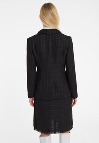Zwarte tweed blazer met een gestructureerd ruitpatroon, voorzien van een notch-kraag, gestructureerde silhouet en een rafelige zoom, gecombineerd met een bijpassende rok.