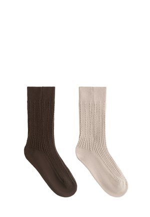 Une chaussette épaisse côtelée marron et une beige présentées côte à côte sur fond blanc.