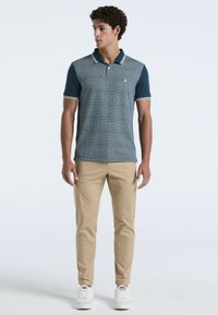 Korte mouwen polo t-shirt in marineblauw met een patroon op het lichaam, in contrast met effen mouwen en kraag. Gecombineerd met beige broeken en witte sneakers.