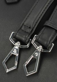 Cinghie in pelle nera con clip in metallo argentato, caratterizzate da una texture liscia e un design elegante, attaccate a uno sfondo scuro.