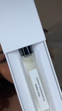 Bottiglia di profumo rettangolare in vetro trasparente con tappo nero, all'interno di un imballaggio bianco. L'etichetta recita "Sandalwood Tempted, Sana Jardin."