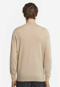 Beige långärmad tröja i mjukt tyg, med rund hals, ribbade ärmslut och nederkant, med en slät textur och enkel design.