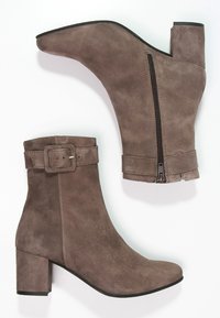 Bottines en suède marron avec un talon block, dotées d'une fermeture éclair sur le côté et d'une sangle décorative à boucle au-dessus de la cheville. Texture lisse, design minimaliste.