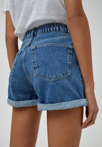 Pantalones cortos de denim de cintura alta, color azul claro, con dobladillos enrollados y dos bolsillos traseros, que cuentan con una cinturilla elástica fruncida.