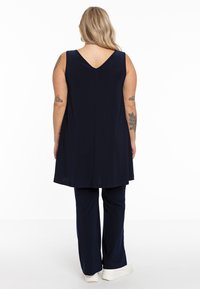 Marineblaue ärmellose Tunika mit V-Rücken, kombiniert mit passenden weit geschnittenen Hosen. Weiche Textur, lässiges Design. Weiße Sneaker runden das Outfit ab.