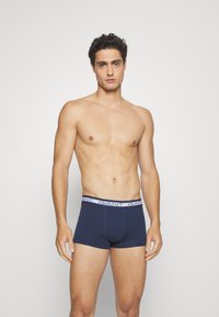 Dark blue boxer briefs with a white logo waistband, made of soft fabric. The design features a snug, fitted cut and minimal stitching details.