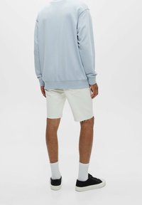 Sudadera azul claro con puños y dobladillo de canalé, combinada con pantalones cortos de mezclilla blancos deshilachados y zapatillas negras con suelas blancas.