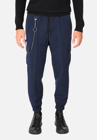 Pantaloni jogger blu navy con vita a coulisse, tasche laterali, polsini elasticizzati e un dettaglio decorativo di una catena argentata sul lato sinistro.