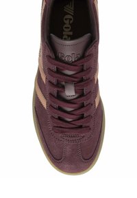 Zapatilla de ante marrón con rayas de acento beige, cordones planos y suela de goma texturizada. Presenta un logotipo de la marca en la lengüeta.