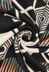 Tessuto a fantasia in bianco e nero con disegni geometrici, caratterizzato da accenti arancioni e verdi. Texture morbida, arrotolato in forma di spirale.