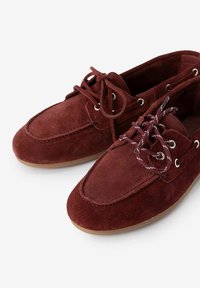 Burgunderfarbene Wildleder-Bootsschuhe mit abgerundetem Zehenbereich, Schnürfront und metallischen Ösen. Strukturiert Oberfläche, weiches Material und braune Außensohle.