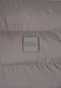 Grå vadderad tyg med sydda horisontella linjer och en centrerad fyrkantig kudde med texten "URBAN CLASSICS."