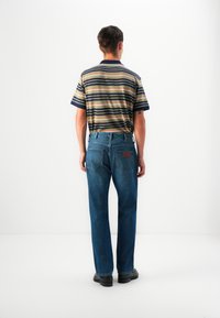 Chemise à manches courtes rayée avec col bleu foncé, associée à un jean droit bleu moyen. Présente des poches arrière et une patch en cuir.