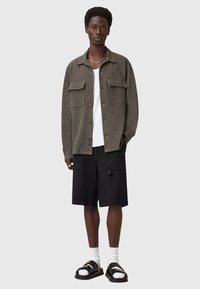 Olive green button-up shirt with two chest pockets, white T-shirt, black cargo shorts, and black sandals with double straps and white socks.