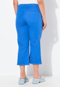 Pantaloni cropped blu con una texture liscia, dotati di due tasche posteriori e una vita elastica. Abbinati a scarpe con tacco a blocco di colore blu chiaro.