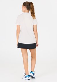 Hvid kortærmet polo og sort atletisk nederdel, parret med blå og hvide sko. Glat materiale, enkelt design og knælang pasform.