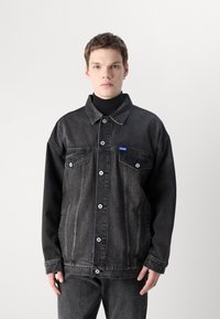 Black denim jacket with a solid color design, featuring button closures, two front pockets, and a small blue logo on the chest.
