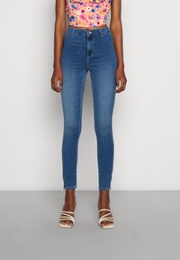 Jeans skinny azuis de cintura alta em denim, com uma textura suave e dois pequenos detalhes em zíper ao nível do tornozelo.