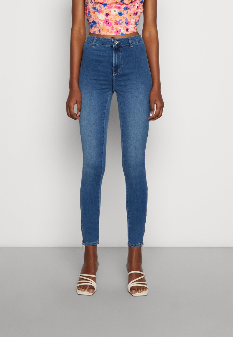 Jeans skinny azuis de cintura alta em denim, com uma textura suave e dois pequenos detalhes em zíper ao nível do tornozelo.