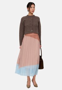 Brown knitted cropped cardigan with round neckline and buttons, paired with a pleated skirt featuring pink and blue gradient colors. Brown handbag.