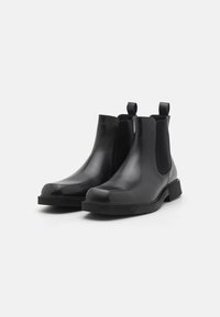 Bottines Chelsea en cuir noir avec panneaux élastiques sur les côtés, bout rond et languettes de tirage. Texture lisse et semelle en caoutchouc plate.