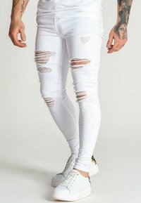 Valkoiset revenneet skinny-farkut, joissa on useita kuluneita kohtia, korostavat tiukkaa muotoilua. Yhdistetty vaaleansävyisten tennareiden kanssa.