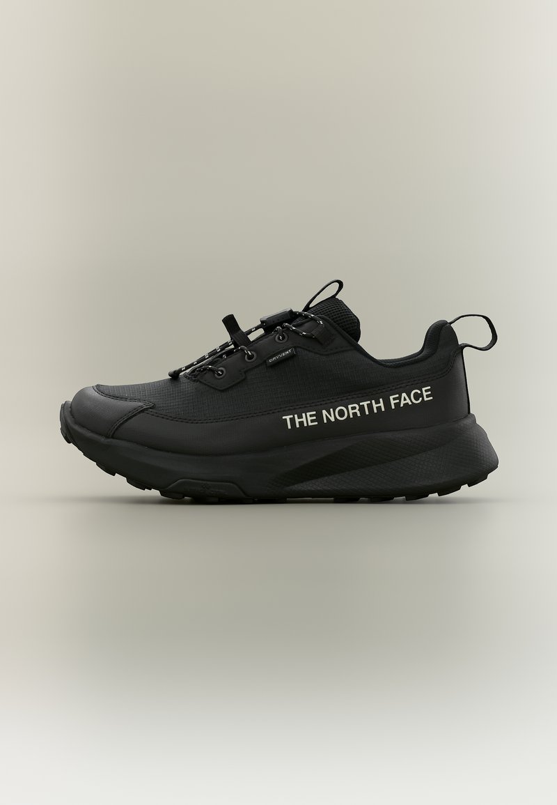 Baskets athlétiques noires avec semelle épaisse, marquées "THE NORTH FACE" sur le côté, dotées de languettes pour faciliter l'enfilage et d'un système de laçage sécurisé avec un toggle.