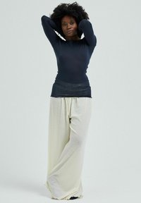 Long-sleeve navy top with a fitted design, paired with loose-fitting cream pants. Both garments have smooth textures and minimal detailing.