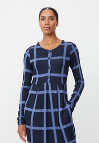 Granatowa sukienka z długim rękawem z jasnoniebieskim wzorem w kratę, okrągłym dekoltem, zapięciem na guziki z przodu i bocznymi kieszeniami. Miękka dzianinowa tkanina z plisowaną spódnicą.