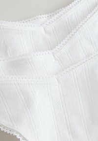 Camisole bianco con rifiniture in pizzo, caratterizzato da un design testurizzato con sottili strisce verticali e motivi a diamante, realizzato in tessuto leggero.