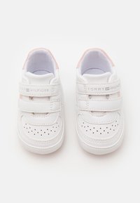 Białe sneakersy z różowymi akcentami, z rzepem, perforowanym wzorem na palcu oraz logo "TOMMY HILFIGER" na boku.