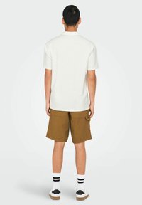 Hvid kortærmet polo-shirt parret med brune shorts, båret med hvide sokker med sorte striber og afslappede sneakers.