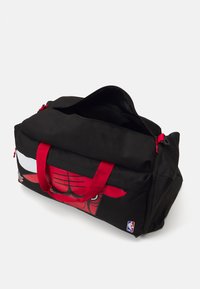 Schwarze Sporttasche mit roten Griffen, die ein grafisches Motiv eines Stiergesichts zeigt. Mit Reißverschlussöffnung und einem NBA-Logopatch an der Seite.
