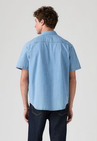 Koszula jeansowa z krótkim rękawem w jasnoniebieskim kolorze, z klasycznym kołnierzem i detalem na tylnej karczku. Gładka struktura i zaokrąglony dół. Połącz z ciemnymi dżinsami.