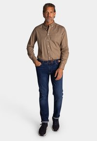 Bruin gemusterd overhemd met knopen, denim spijkerbroek en zwarte sneakers. Het overhemd heeft een kraag en een borstzak, terwijl de spijkerbroek een slim fit heeft.