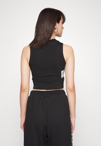 Fekete, ujjatlan crop top pamutból, kerek nyakkivágással és egy kis szőtt címkével a hátán. Fekete nadrággal párosítva.