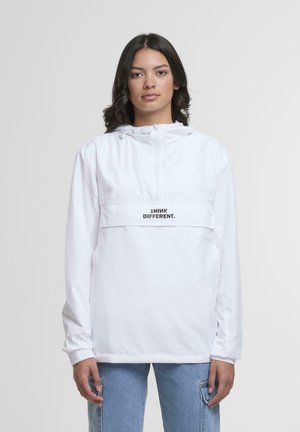 Woman with dark hair wears white hooded jacket with "THINK DIFFERENT." text, paired with blue jeans against plain light background.