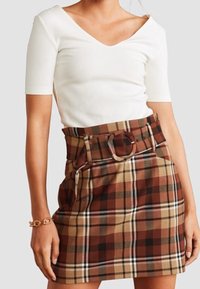 Top blanco de manga corta acanalado combinado con una falda de cuadros marrón de cintura alta que incluye cinturón, bolsillos laterales y un patrón de cuadros.