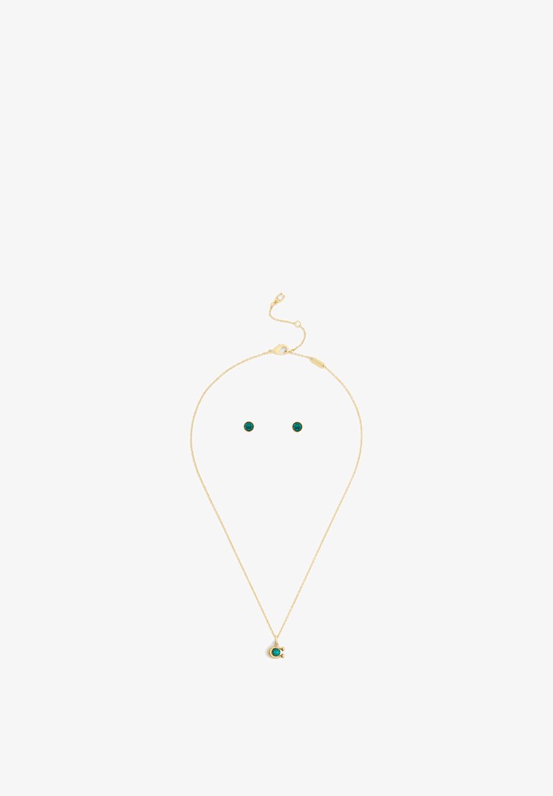 Collier en or et ensemble de clous d'oreilles assortis avec des pierres précieuses vertes rondes sur fond blanc.