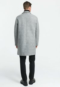 Hall hallitatud hallitatud mantel, millel on struktureeritud disain ja punktsabber, koos mustade pükste ja kingadega. Vaade tagant.