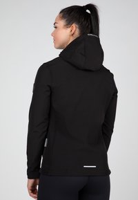 Melns kapucis džemperis no mīksta, elastīga materiāla. Funkcijas ietver logotipu uz muguras, piegulošu dizainu un atstarotājus gar apakšmalu.