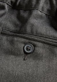 Tissu en denim noir avec un bouton visible et un petit détail de poche, présentant un tissage texturé et une apparence légèrement délavée.