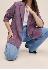 Blazer à motif pied-de-poule violet et noir avec une coupe ajustée, associé à un jean taille haute bleu clair et des bottines à talons noires.