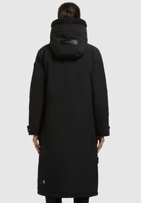 Crni dugi kaput s teksturiranim, plišanim kapuljačom i glatkim vanjskim materijalom. Ima logotip na leđima i manžetne na gumb.