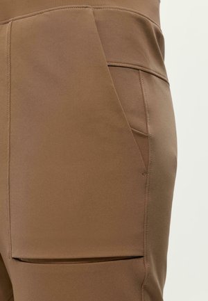 Brūni bikses, kas izgatavotas no elastīga auduma, ar sānu kabatām, gludu tekstūru un pieguļošu jostu.